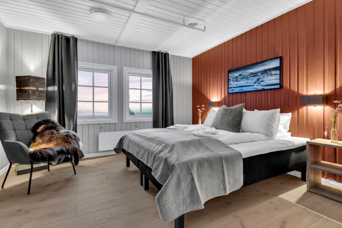Soverom med rustrød panelvegg, dobbeltseng og utsikt mot solnedgang